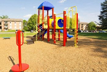 a colorful playground in a park with apartment buildings in the background at Fairbrook Park Apartments in Baltimore, MD